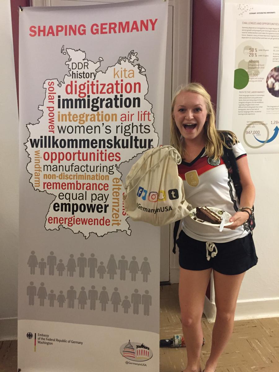 A student enjoys cake and shows off a swag bag at the Integrating Immigrants exhibit